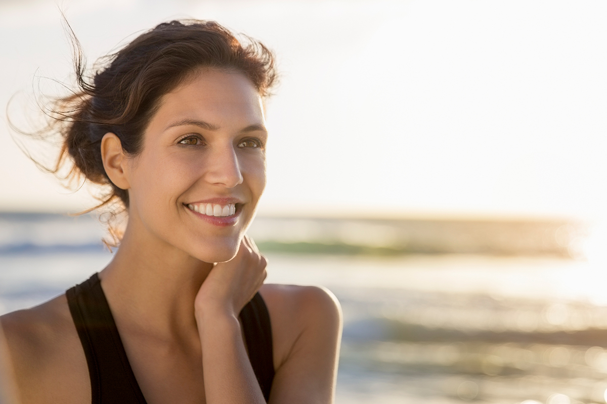 a woman standing in front of a body of water smiling as the sun rises before getting laser skin resurfacing in Sarasota